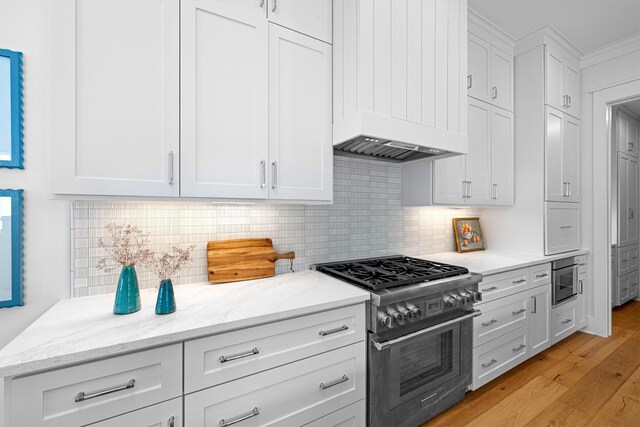 2604 E Seaside Dr, Galveston, TX 77550 - kitchen with stainless steel stove, white cabinetry, light wood finished floors, premium range hood, and light stone counters