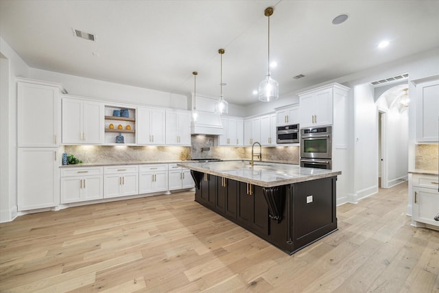 19 Sanctuary Trl, Missouri City, TX 77459 - kitchen with stainless steel double oven, white cabinetry, arched walkways, tasteful backsplash, and light wood finished floors