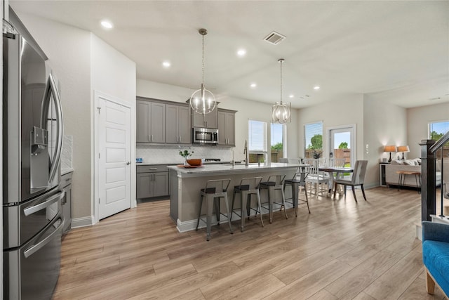 29510 Enchanted Breeze Ln, Katy, TX 77494 - kitchen featuring appliances with stainless steel finishes, gray cabinets, open floor plan, a breakfast bar area, and light wood finished floors