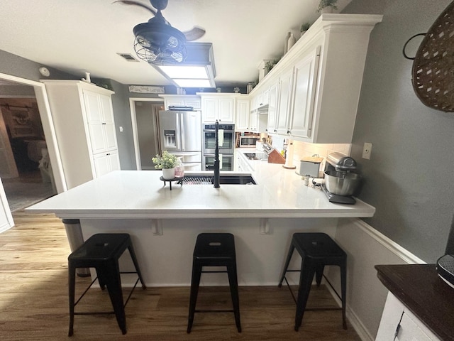 1308 Hagan St, Crockett, TX 75835 - kitchen featuring appliances with stainless steel finishes, a peninsula, light wood-style floors, a kitchen bar, and white cabinetry