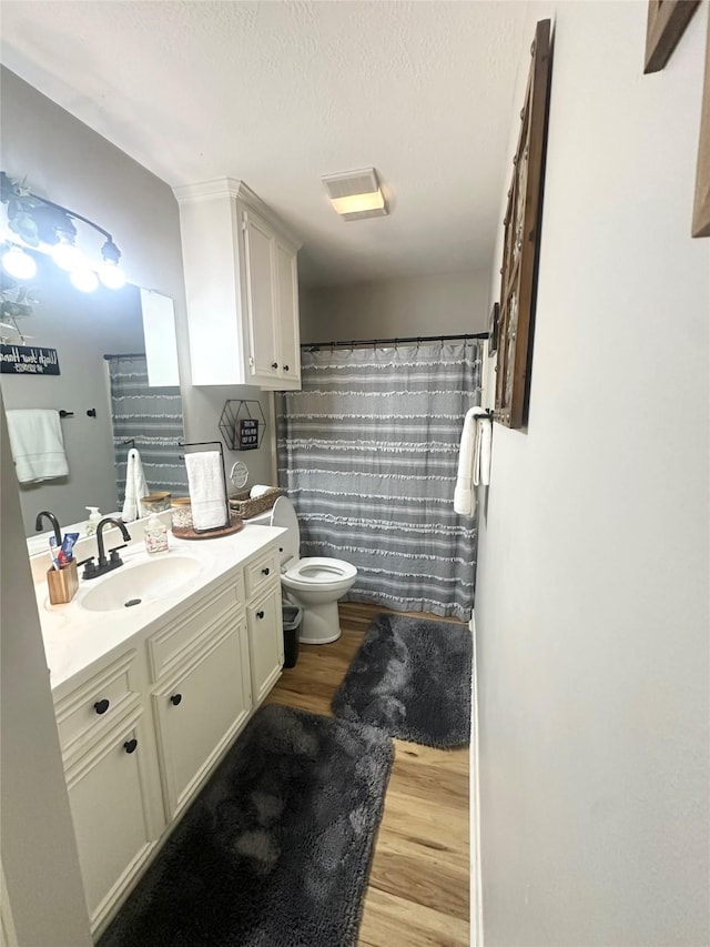 1308 Hagan St, Crockett, TX 75835 - bathroom with wood finished floors, toilet, vanity, a textured ceiling, and a shower with shower curtain