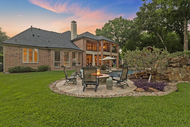 77 Big Trl, Missouri City, TX 77459 - back of property at dusk featuring a patio area, an outdoor fire pit, a chimney, brick siding, and a yard