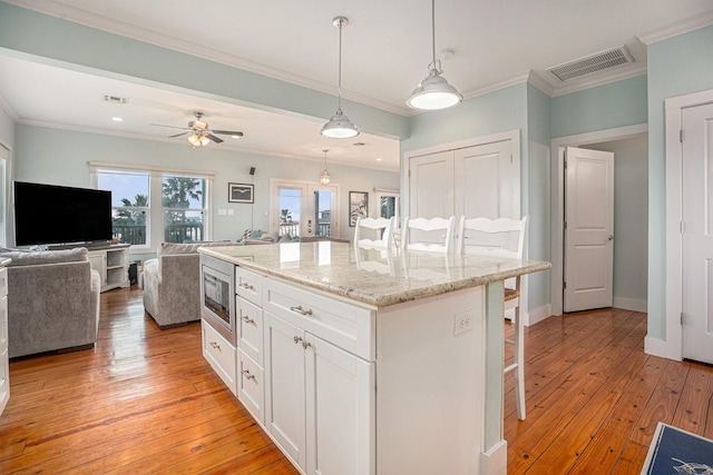 1401 103rd St, Galveston, TX 77554 - kitchen featuring a breakfast bar area, open floor plan, white cabinetry, stainless steel microwave, and ornamental molding