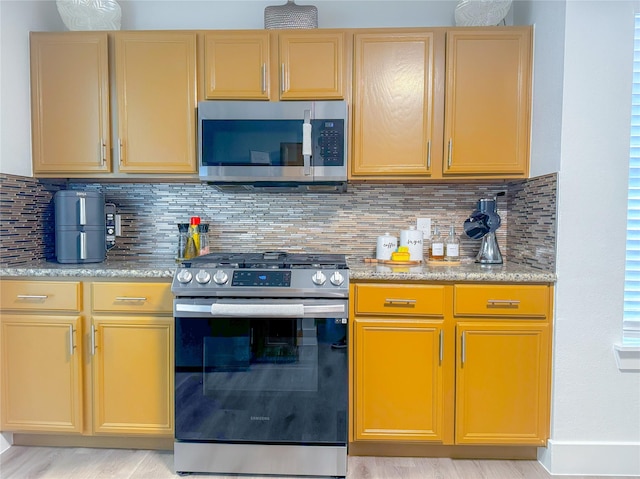 18323 River Sage Dr, Houston, TX 77084 - kitchen featuring appliances with stainless steel finishes, decorative backsplash, light stone counters, and light wood-type flooring