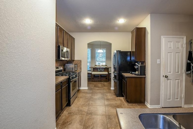 11019 Chestnut Path Way, Tomball, TX 77375 - kitchen with appliances with stainless steel finishes, arched walkways, dark brown cabinetry, light tile patterned flooring, and recessed lighting