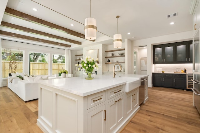 1611 Richelieu Ln, Houston, TX 77018 - kitchen featuring an island with sink, light wood-type flooring, recessed lighting, beamed ceiling, and glass insert cabinets