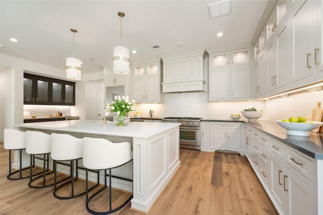1611 Richelieu Ln, Houston, TX 77018 - kitchen featuring stainless steel stove, custom exhaust hood, tasteful backsplash, a kitchen island with sink, and light wood-style floors