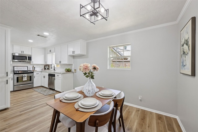 1008 N 30th St, Nederland, TX 77627 - dining space featuring a textured ceiling, light wood-style flooring, crown molding, a chandelier, and baseboards