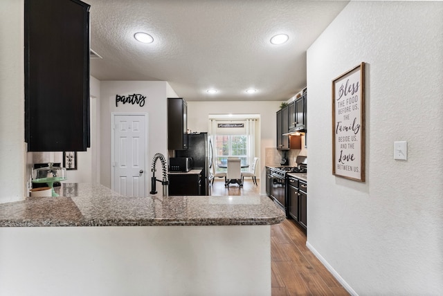 14706 Meadow Acre Trl, Houston, TX 77049 - kitchen featuring black gas range, a textured ceiling, a textured wall, wood finished floors, and a peninsula