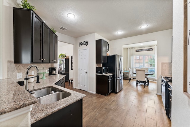 14706 Meadow Acre Trl, Houston, TX 77049 - kitchen featuring a sink, dark cabinets, stainless steel appliances, light wood finished floors, and light stone counters