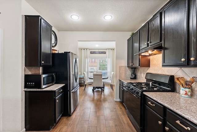 14706 Meadow Acre Trl, Houston, TX 77049 - kitchen featuring stainless steel appliances, under cabinet range hood, dark cabinetry, decorative backsplash, and a textured ceiling