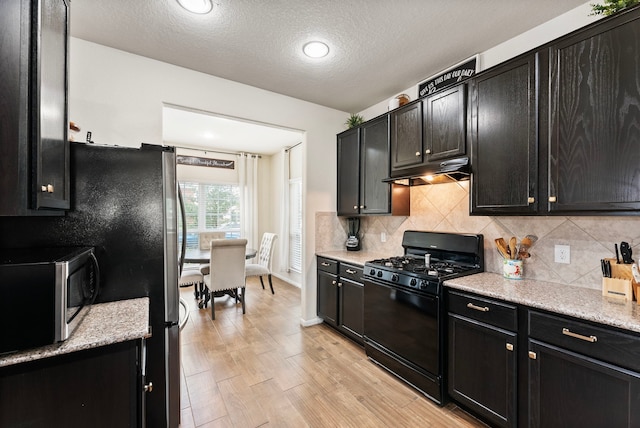 14706 Meadow Acre Trl, Houston, TX 77049 - kitchen featuring gas stove, stainless steel microwave, under cabinet range hood, dark cabinetry, and a textured ceiling