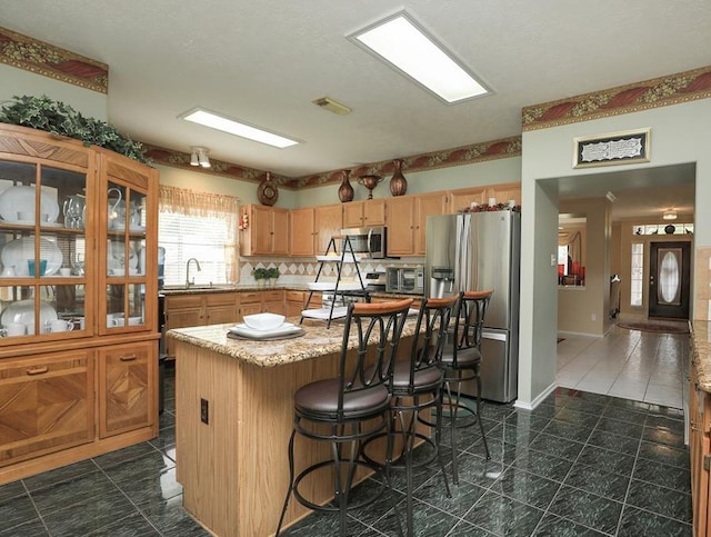 4915 Dove Springs Dr, Houston, TX 77066 - kitchen with stainless steel appliances, a sink, a kitchen breakfast bar, light brown cabinetry, and light stone countertops