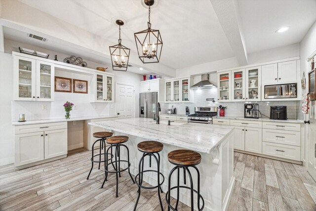 529 Fugate St, Houston, TX 77009 - kitchen featuring stainless steel appliances, wall chimney range hood, backsplash, light wood-style flooring, and beamed ceiling