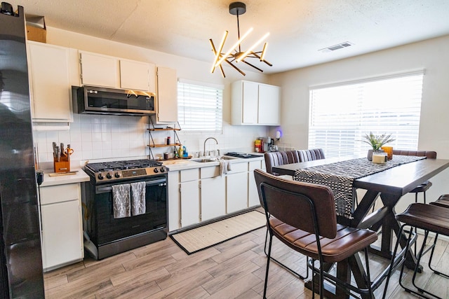 326 W 28th St, Houston, TX 77008 - kitchen with stainless steel appliances, light countertops, tasteful backsplash, light wood-style floors, and a chandelier