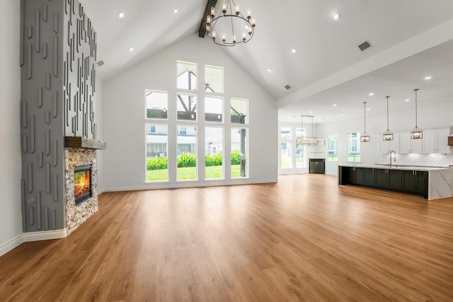 243 Teewood Ct, Montgomery, TX 77356 - unfurnished living room featuring a stone fireplace, a chandelier, light wood-style flooring, beam ceiling, and high vaulted ceiling