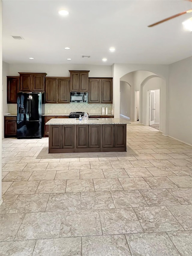 3328 Primrose Canyon Ln, Pearland, TX 77584 - kitchen with black appliances, arched walkways, backsplash, a kitchen island, and dark brown cabinetry