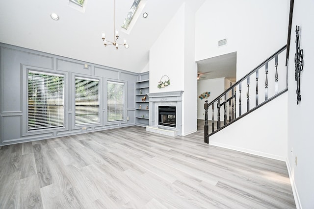 31 Silent Brook Pl, The Woodlands, TX 77381 - unfurnished living room with high vaulted ceiling, stairs, built in features, light wood-style flooring, and a chandelier
