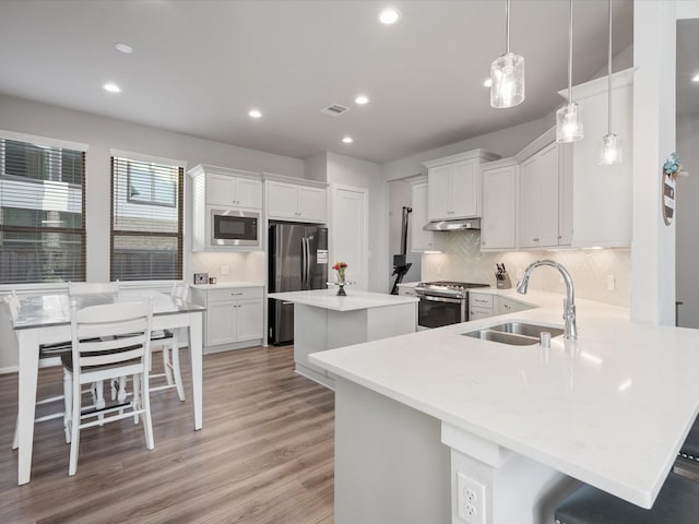 9715 Migrant Hawker Ct, Conroe, TX 77385 - kitchen with appliances with stainless steel finishes, a sink, under cabinet range hood, a kitchen island, and decorative backsplash