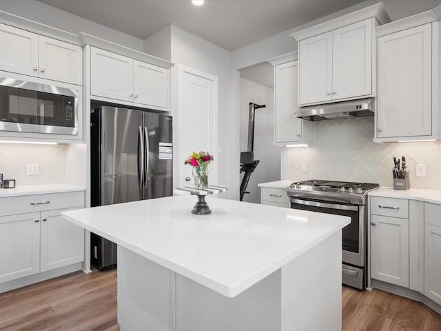 9715 Migrant Hawker Ct, Conroe, TX 77385 - kitchen with stainless steel appliances, under cabinet range hood, tasteful backsplash, light countertops, and a center island