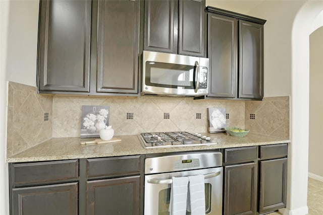 19538 Salt Grass Meadow Dr, Cypress, TX 77433 - kitchen with appliances with stainless steel finishes, arched walkways, decorative backsplash, baseboards, and light stone counters