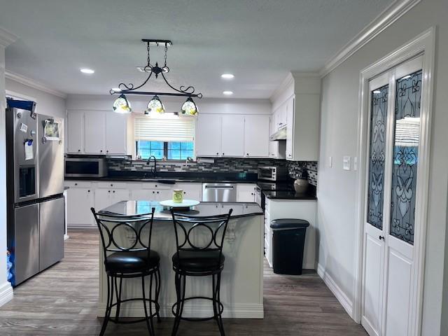 8594 Morgan Ln, Orange, TX 77632 - kitchen featuring appliances with stainless steel finishes, dark countertops, ornamental molding, white cabinetry, and wood finished floors