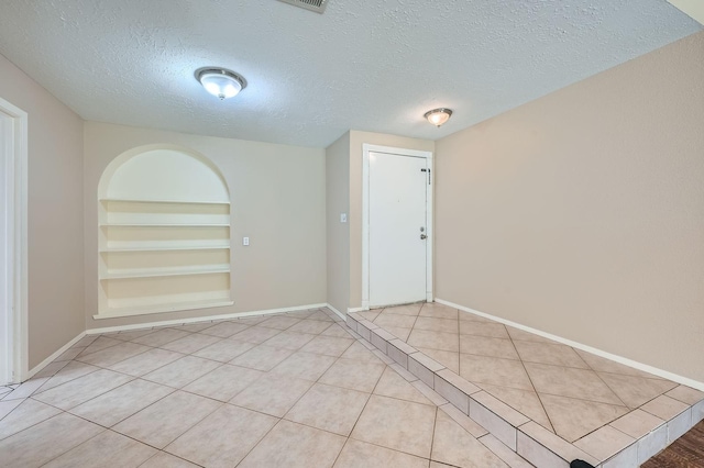 9519 Landry Blvd, Spring, TX 77379 - empty room with built in shelves, a textured ceiling, baseboards, and tile patterned floors