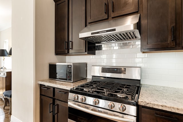 1221 W 25th St Unit D, Houston, TX 77008 - kitchen featuring ventilation hood, appliances with stainless steel finishes, dark brown cabinetry, decorative backsplash, and light stone counters