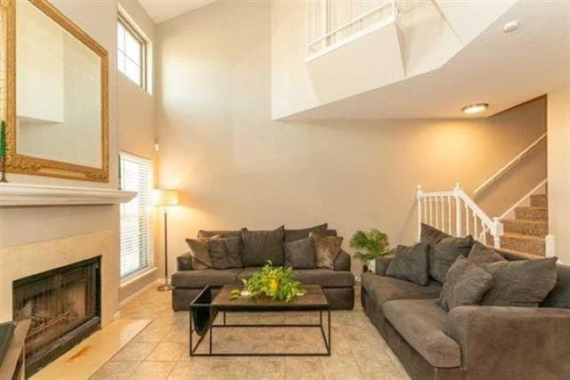 1620 Wellington Pl Unit 303, Beaumont, TX 77706 - living area featuring a towering ceiling, a fireplace, stairs, light tile patterned floors, and baseboards
