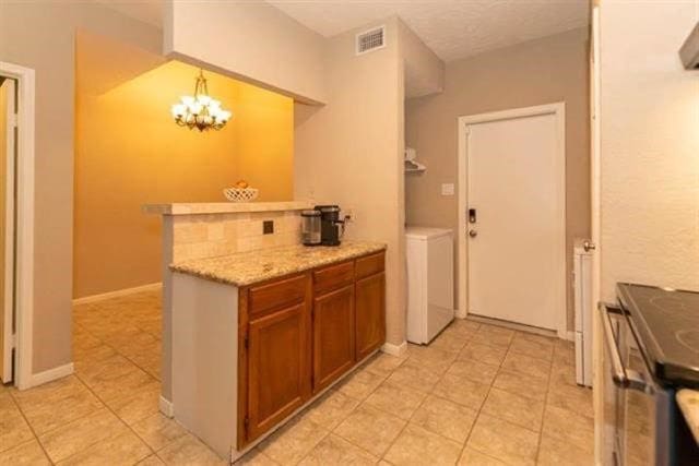 1620 Wellington Pl Unit 303, Beaumont, TX 77706 - kitchen with washer / dryer, light tile patterned floors, brown cabinetry, a chandelier, and decorative light fixtures