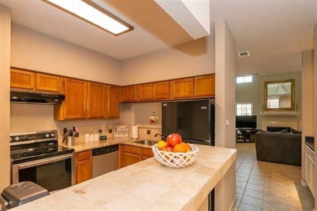 1620 Wellington Pl Unit 303, Beaumont, TX 77706 - kitchen with stainless steel appliances, under cabinet range hood, tile counters, brown cabinets, and tile patterned flooring