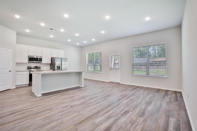 1452 Glenoaks Dr, Conroe, TX 77385 - kitchen featuring appliances with stainless steel finishes, light wood-type flooring, a kitchen island with sink, open floor plan, and white cabinets