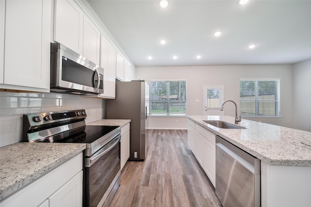 1452 Glenoaks Dr, Conroe, TX 77385 - kitchen featuring appliances with stainless steel finishes, a sink, light wood finished floors, white cabinets, and a center island with sink