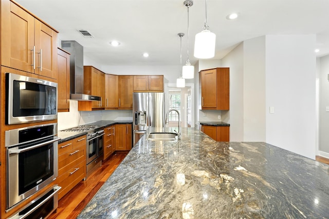 263 S Crimson Clover Ct, The Woodlands, TX 77381 - kitchen featuring stainless steel appliances, wall chimney range hood, brown cabinetry, dark stone counters, and pendant lighting