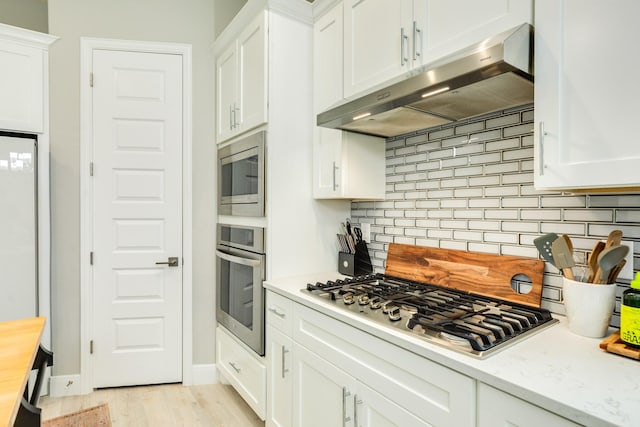 9715 Highland Pointe Dr, Needville, TX 77461 - kitchen with appliances with stainless steel finishes, under cabinet range hood, backsplash, white cabinetry, and light wood-style floors
