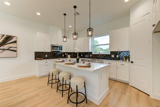 4045 Buck St, Houston, TX 77020 - kitchen with stainless steel microwave, light wood-type flooring, a breakfast bar, backsplash, and recessed lighting