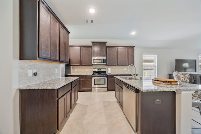 23715 Rivage Ridge Dr, Katy, TX 77493 - kitchen with stainless steel appliances, a sink, decorative backsplash, dark brown cabinetry, and light stone counters