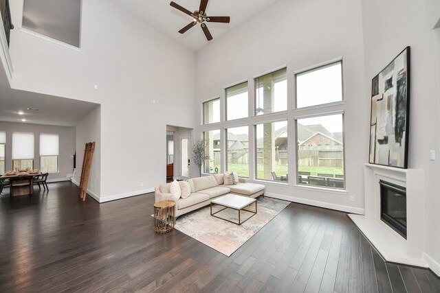 12813 N Palomino Lake Cir, Cypress, TX 77429 - living area featuring a glass covered fireplace, a high ceiling, dark wood-type flooring, a ceiling fan, and baseboards