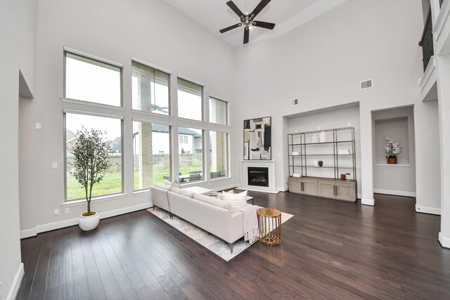 12813 N Palomino Lake Cir, Cypress, TX 77429 - living area with a ceiling fan, a glass covered fireplace, baseboards, a towering ceiling, and dark wood-style floors