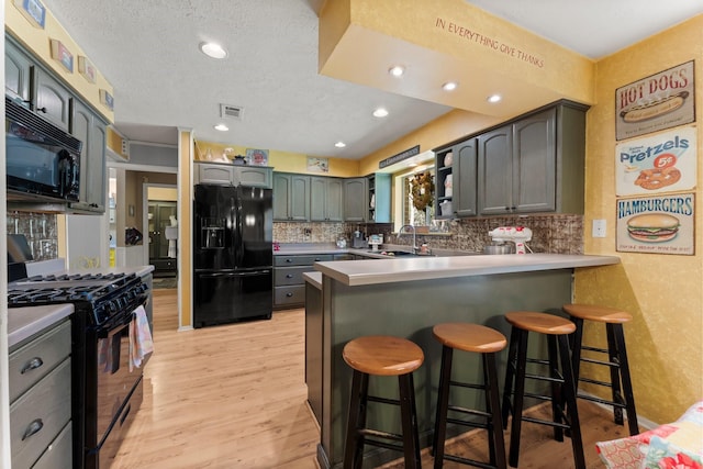 3027 Pine Acres Dr, Conroe, TX 77384 - kitchen featuring black appliances, a peninsula, a sink, light wood-style floors, and recessed lighting