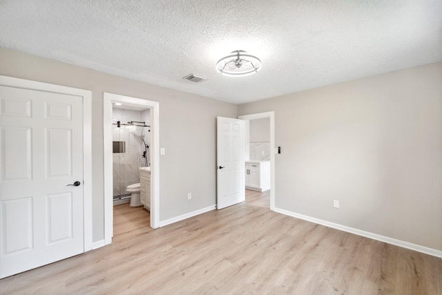 11114 Daybreak Ln, Cypress, TX 77429 - unfurnished bedroom featuring light wood-type flooring, baseboards, a textured ceiling, and connected bathroom