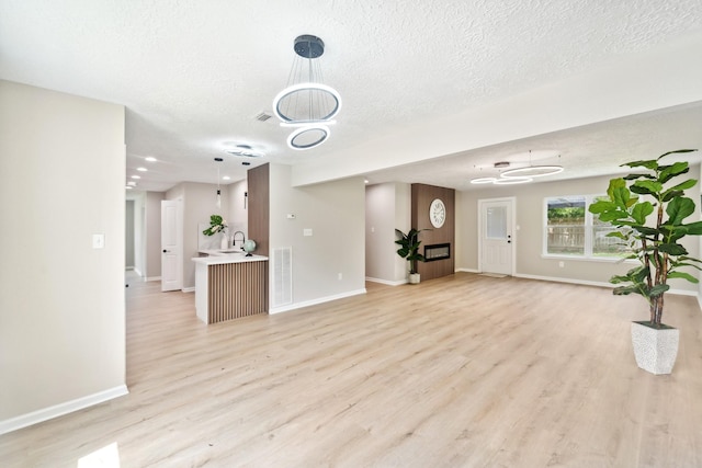 11114 Daybreak Ln, Cypress, TX 77429 - unfurnished living room with light wood finished floors, baseboards, a textured ceiling, a sink, and a chandelier