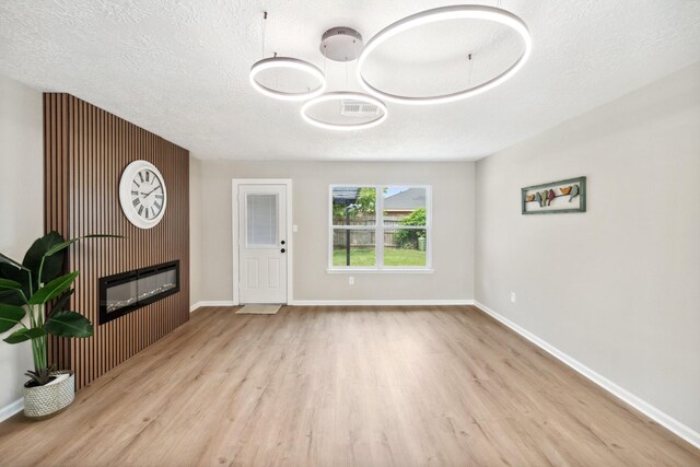 11114 Daybreak Ln, Cypress, TX 77429 - unfurnished living room with wood finished floors, a glass covered fireplace, baseboards, and a textured ceiling