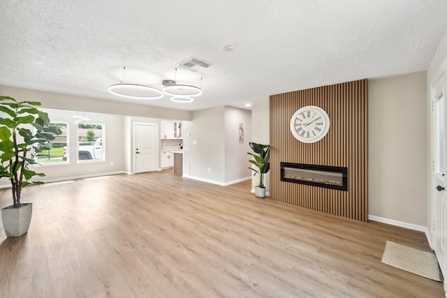 11114 Daybreak Ln, Cypress, TX 77429 - unfurnished living room with light wood finished floors, baseboards, a glass covered fireplace, and a textured ceiling