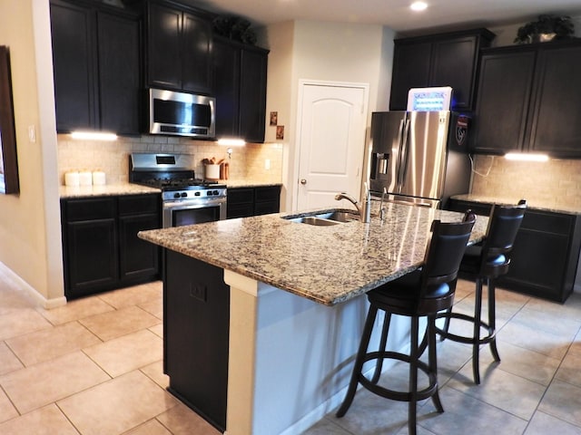 2705 Osprey Ln, Pearland, TX 77581 - kitchen with appliances with stainless steel finishes, dark cabinets, light stone counters, a sink, and tasteful backsplash