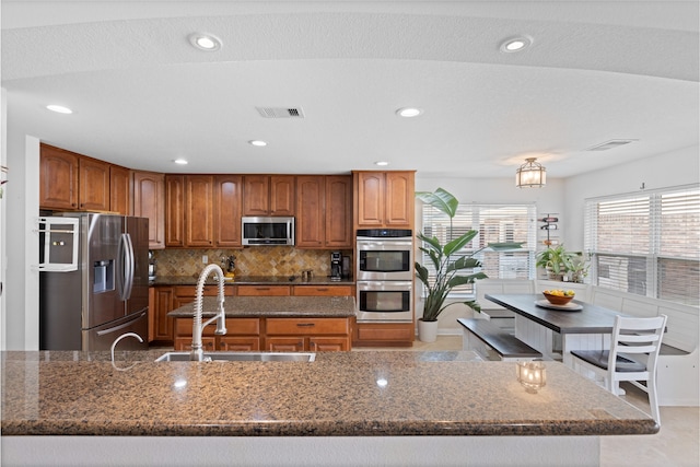 10711 Indian Trails Dr, Tomball, TX 77375 - kitchen with stainless steel appliances, a sink, dark stone counters, brown cabinets, and recessed lighting