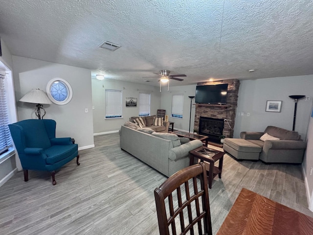 219 Lakeside Dr, Kemah, TX 77565 - living area featuring a stone fireplace, wood finished floors, a textured ceiling, a ceiling fan, and baseboards