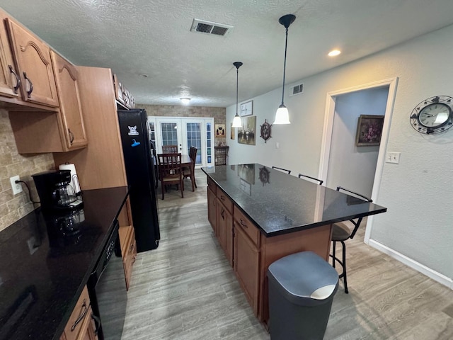 219 Lakeside Dr, Kemah, TX 77565 - kitchen featuring light wood-type flooring, black appliances, a breakfast bar, a center island, and a textured ceiling