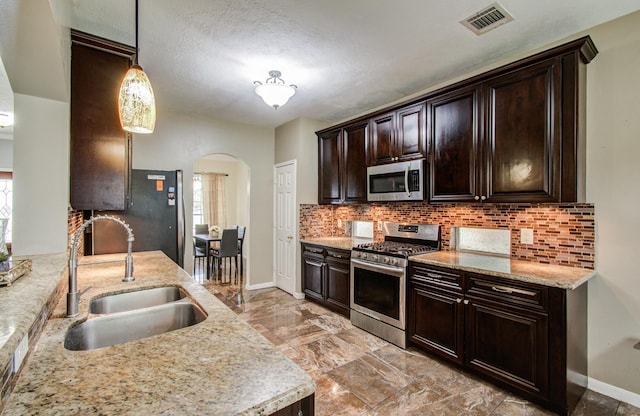 3203 Blaesser Dr, Pearland, TX 77584 - kitchen featuring appliances with stainless steel finishes, a sink, arched walkways, dark brown cabinetry, and backsplash