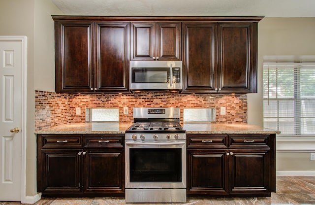 3203 Blaesser Dr, Pearland, TX 77584 - kitchen featuring appliances with stainless steel finishes, light stone countertops, backsplash, dark brown cabinets, and baseboards